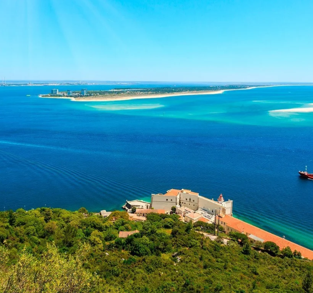 Vista panorâmica da Região Vínica Península de Setúbal com mar azul e vegetação ao redor.
