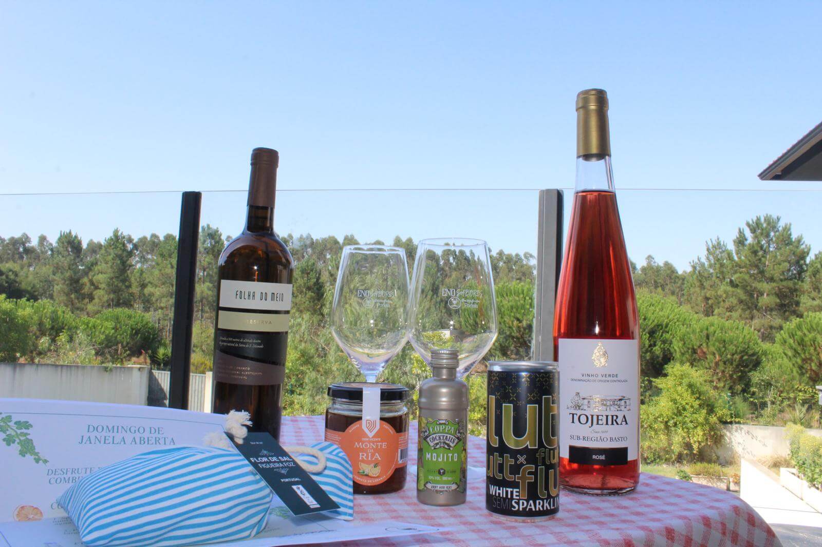 Kit Domingo Sem Pressa featuring wine, glasses, and gourmet items on a table with nature backdrop.