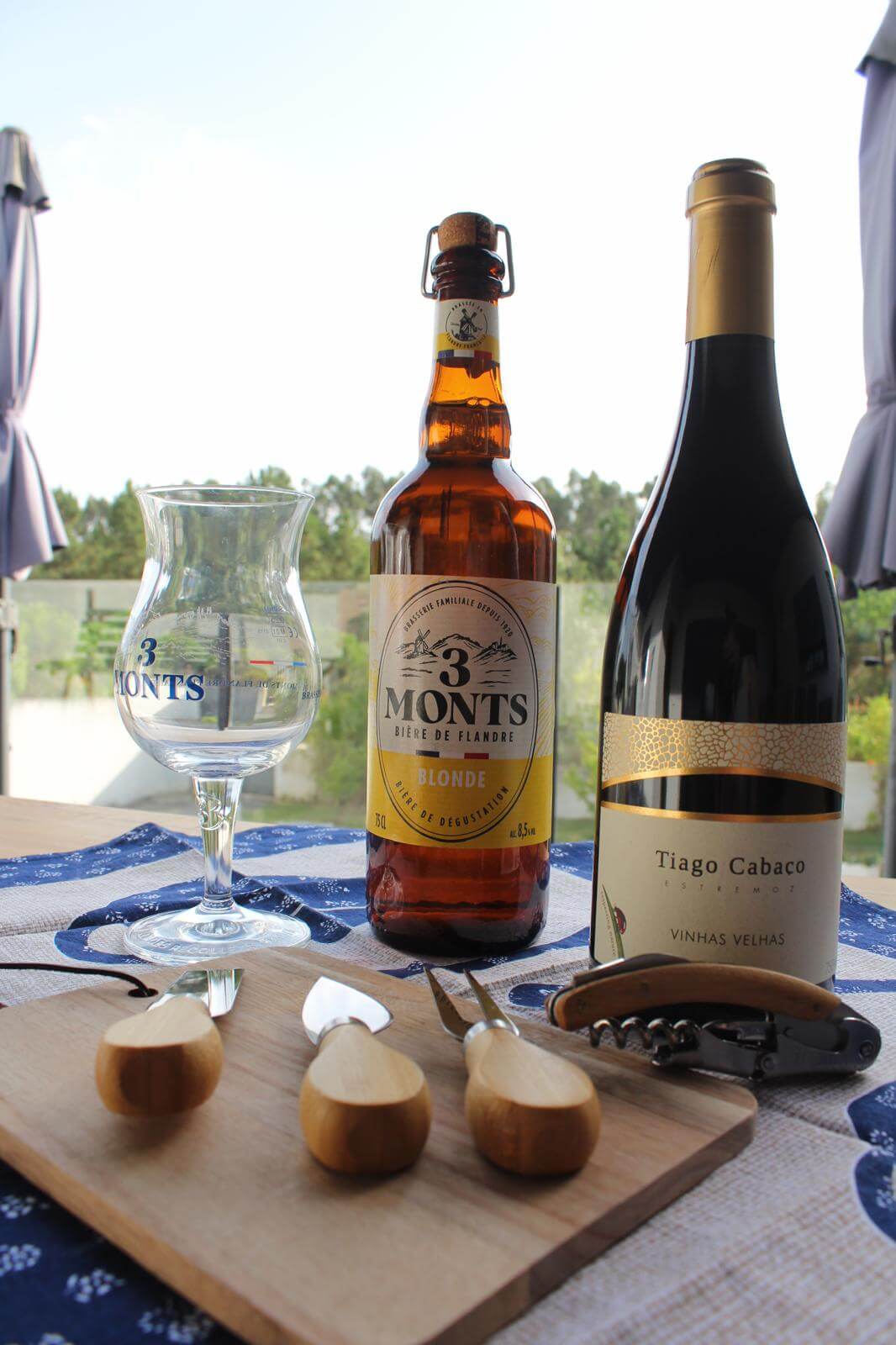 3 Monts beer bottle, Tiago Cabaco wine, glass, and corkscrew on a wooden board.
