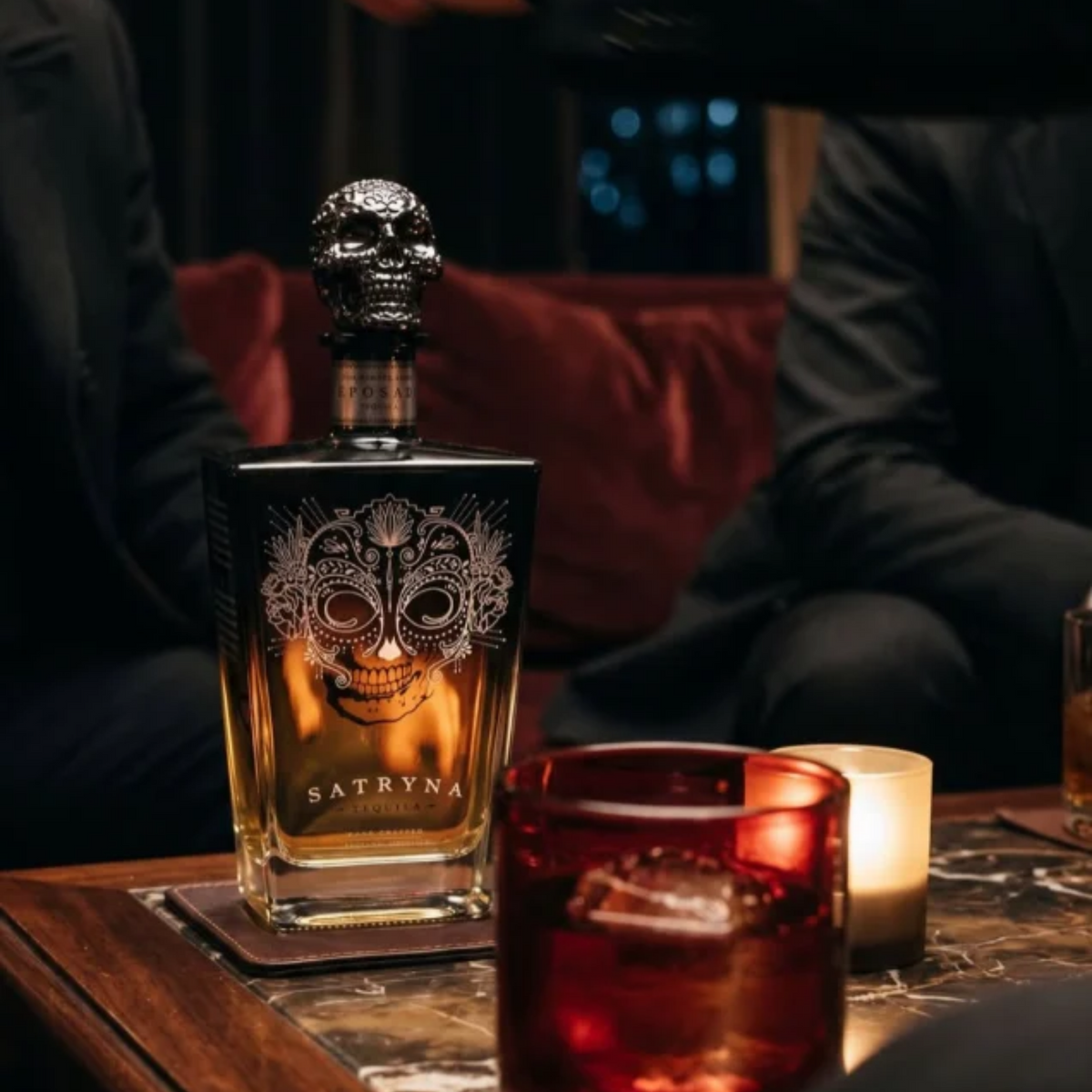 Garrafa de Satryna Tequila Reposado 0.70 38% em mesa com copos e velas.